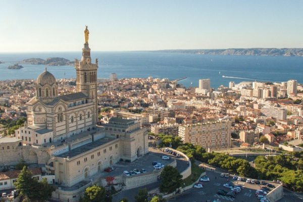 High angle view of cityscape by sea. Notre Dame de la Garde in Marseille against clear sky. Buildings by seascape on sunny day.