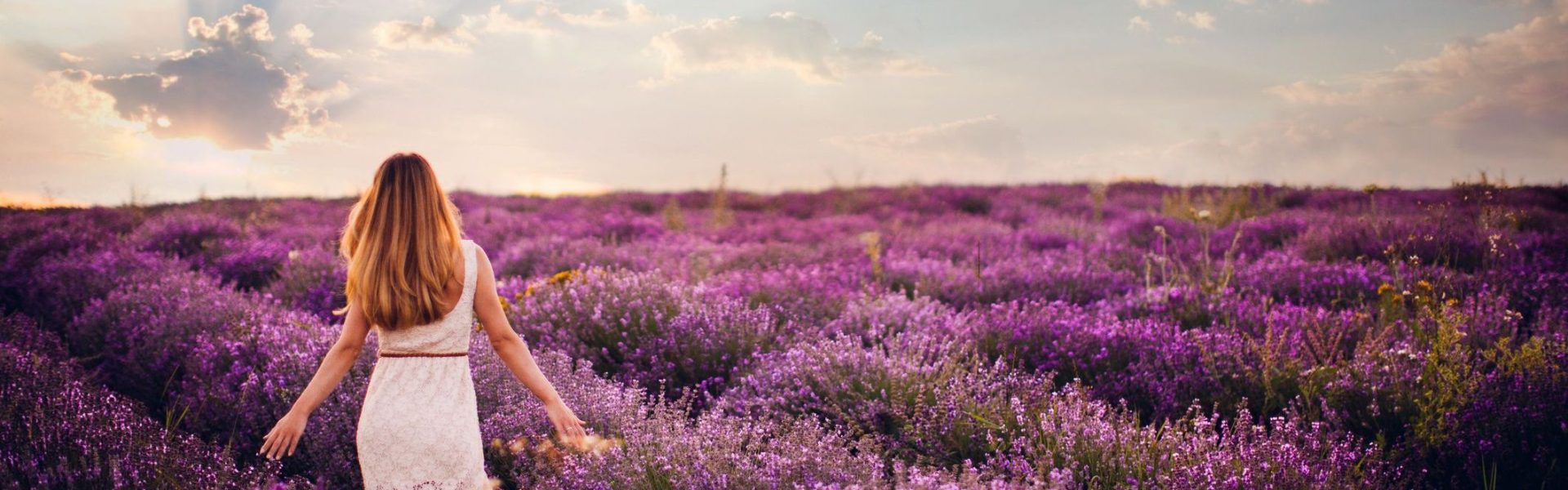 Photo of a young woman with arms outstretched walking down the lavender field, enjoying life