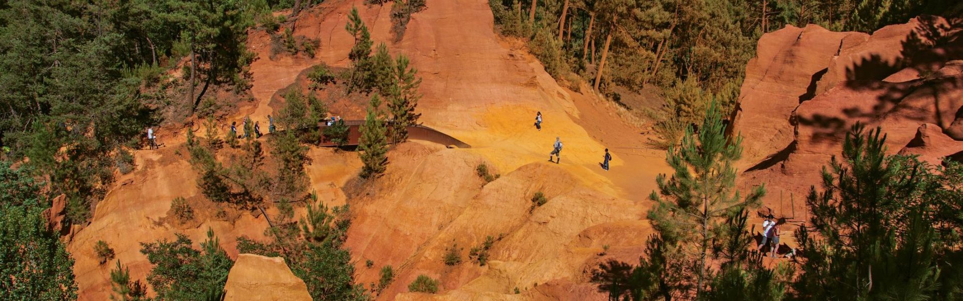 Roussillon, France - July 03, 2016. View of ocher land and people in the park "Sentiers des Ocres" under a sunny blue sky, near the village of Roussillon. Located in the Vaucluse department, Provence region, in southeastern France